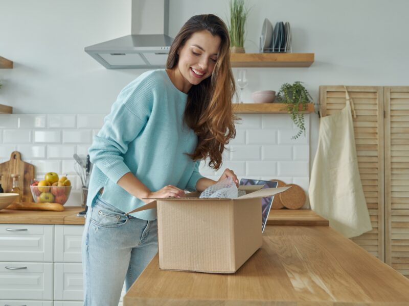 Beautiful,Young,Woman,Unpacking,Box,While,Standing,At,The,Domestic